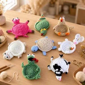 May include: A collection of handmade crochet animal coasters, including a pink pig, green frog, white sheep, blue turtle, and a white rabbit. The coasters are arranged on a light brown wooden surface, showcasing their unique designs and textures.