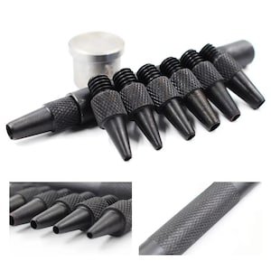 May include: A set of black metal leather hole punch tools featuring a knurled grip texture for manual operation. The collection includes multiple interchangeable punch tips of varying sizes and a single silver-toned cylindrical metal base component.