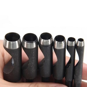May include: A set of six cylindrical metal hollow punches arranged in descending order of size. Each tool features a dark grey matte finish with a polished silver-toned circular cutting edge at the top and a side opening for debris removal.