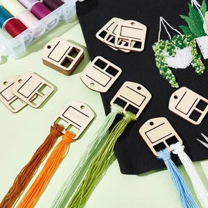 以下が含まれることがあります： 長方形の切り抜きと上部に穴が開いた、明るい色の木製刺繍糸巻きのコレクション。いくつかの糸巻きは空ですが、他の糸巻きには茶色、オレンジ、緑、水色、白の刺繍糸が巻かれています。