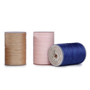 May include: Three cylindrical spools of sewing thread in tan, light pink, and dark blue. The blue spool is positioned horizontally, displaying a white label with the text 0.55mm and 137, while the tan and pink spools stand vertically upright.