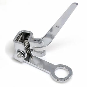 May include: A silver-colored metal sewing machine presser foot attachment featuring a hinged mechanism with a coiled spring, a vertical lever arm, and a flat base plate with a circular opening at the end for needle clearance during operation.