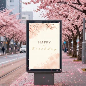Op de afbeelding: Een digitaal bord met de tekst "HAPPY - Birthday" in gouden letters. De achtergrond is zachtroze met kersenbloesemaccenten. De scène toont een straat met bloeiende kersenbomen.