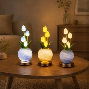 Peut inclure: Trois lampes en forme de tulipes avec des bases sphériques. La lampe de gauche a une base aux tourbillons bleus et une lumière blanche froide. Celle du centre a une base jaune et une lumière chaude. Celle de droite a une base bleue et une lumière chaude.