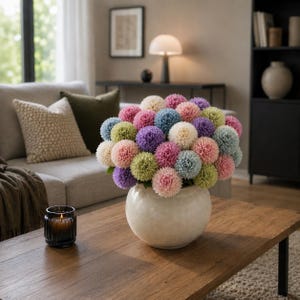 Peut inclure: Un bouquet de fleurs sphériques multicolores, roses, bleues, violettes et vertes, dans un vase rond crème. Le vase est posé sur une table basse en bois, avec une bougie allumée dans un pot en verre. Un canapé et une lampe sont en arrière-plan.