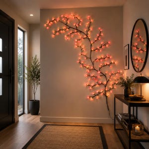 Puede incluir: Una luz decorativa de pared con forma de rama, que presenta un tallo oscuro y sinuoso adornado con numerosas pequeñas luces LED en forma de flor de color rosa y naranja que iluminan la pared con un patrón orgánico y ramificado.