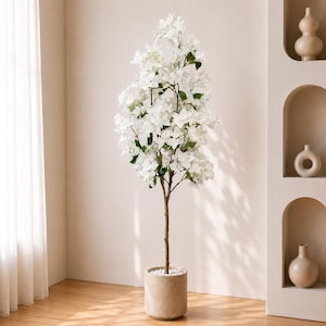 Peut inclure: Un bougainvillier artificiel avec des fleurs blanches et des feuilles vertes. L'arbre est dans un pot cylindrique beige rempli de galets blancs. Le tronc brun de l'arbre soutient les fleurs blanches. Le pot mesure environ 30 cm de diamètre.
