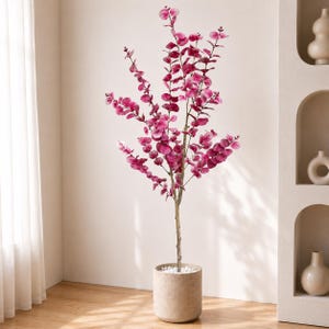 May include: A tall, artificial eucalyptus plant with vibrant magenta leaves. The plant stands in a cylindrical, beige pot filled with small white stones. The plant's slender, brown trunk rises from the pot, branching out into multiple stems.