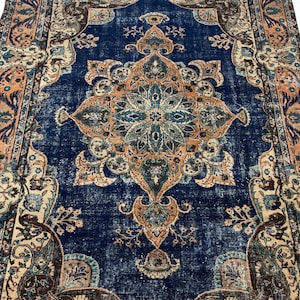 May include: A rectangular area rug featuring a deep blue central field with a large, intricate floral medallion in shades of orange, teal, and cream. The border displays a repeating pattern of ornate botanical motifs in matching colors.