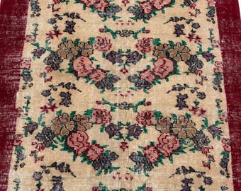 May include: A rectangular runner rug featuring a beige centre field with a repeating floral pattern in shades of pink, brown, purple, and green. The rug is framed by wide, solid deep red borders along both long vertical edges.