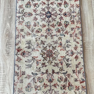 May include: A rectangular, vintage-style rug with an intricate floral pattern in cream, red, blue, and green. The rug's design features a central medallion and repeating floral motifs. The rug is placed on a light-colored wooden floor.