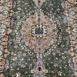 May include: A rectangular area rug featuring a central medallion design in shades of olive green, muted orange, and soft lavender. The intricate pattern includes floral motifs and geometric borders with a distressed, weathered texture throughout.