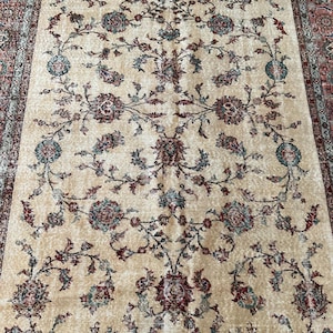 May include: A rectangular area rug featuring a cream-colored field with a symmetrical floral vine pattern in shades of deep red, muted blue, and sage green. The rug is framed by a wide border with intricate floral motifs in matching colors.