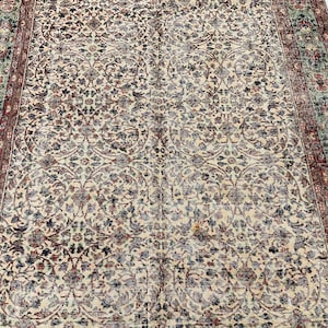 May include: A rectangular area rug featuring a cream-colored field with an intricate, repeating floral vine pattern in shades of dark blue, red, and sage green. The border consists of a wide band with floral motifs in red and green tones.