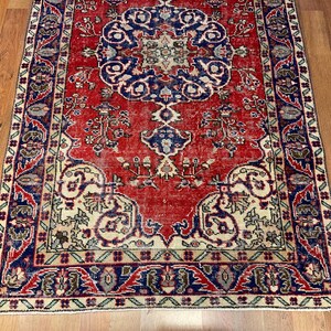 Pu&ograve; includere: Un tappeto rettangolare caratterizzato da un campo rosso vivace con un grande medaglione centrale blu. Il design include intricati motivi floreali e geometrici in tonalit&agrave; crema, blu navy e verde tenue, incorniciati da un bordo decorativo.