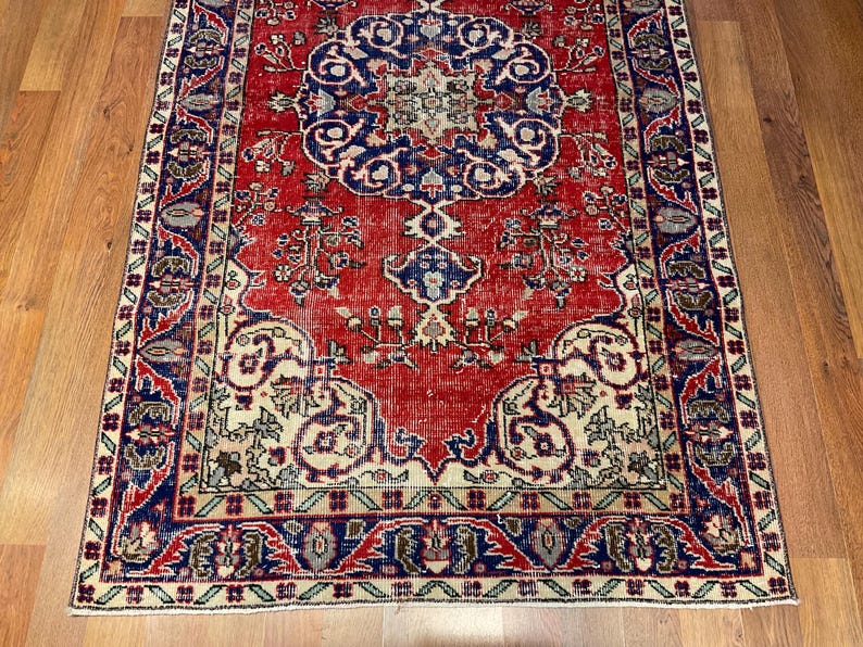 Pu&ograve; includere: Un tappeto rettangolare caratterizzato da un campo rosso vivace con un grande medaglione centrale blu. Il design include intricati motivi floreali e geometrici in tonalit&agrave; crema, blu navy e verde tenue, incorniciati da un bordo decorativo.