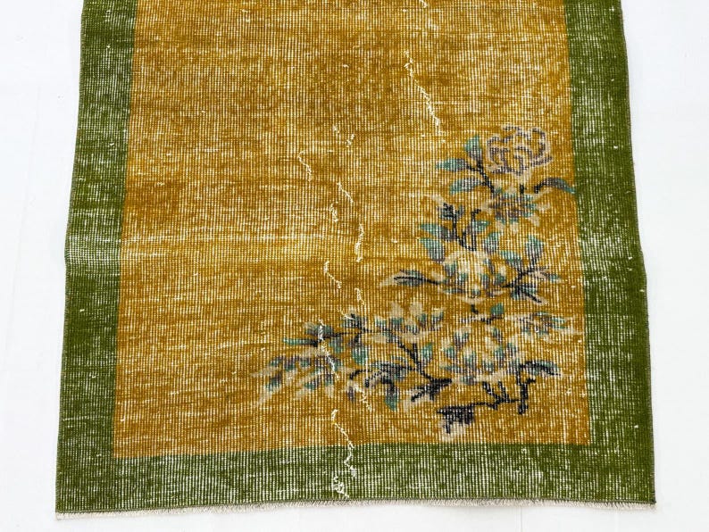 May include: A rectangular rug featuring a mustard yellow centre field with a distressed texture and a floral motif in shades of blue, white, and green. The rug is framed by a solid dark green border on all sides, showcasing a woven textile construction.