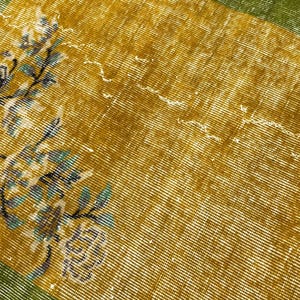 May include: A rectangular textile featuring a mustard yellow centre with a white and teal floral pattern on the left side. The fabric is framed by a solid olive green border on the top and bottom edges, showcasing a woven texture throughout.