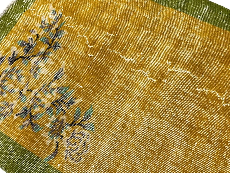May include: A rectangular textile featuring a mustard yellow centre with a white and teal floral pattern on the left side. The fabric is framed by a solid olive green border on the top and bottom edges, showcasing a woven texture throughout.