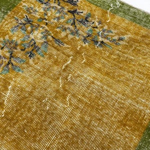 May include: A rectangular textile featuring a mustard yellow centre field with a floral pattern in shades of blue, green, and white. The fabric has a wide, solid green border along the edges, showcasing a woven texture with visible wear.