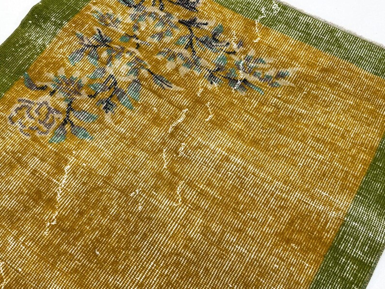 May include: A rectangular textile featuring a mustard yellow centre field with a floral pattern in shades of blue, green, and white. The fabric has a wide, solid green border along the edges, showcasing a woven texture with visible wear.