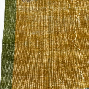 May include: A woven textile rug featuring a mustard yellow central field with a distinct vertical green border along the left edge. The surface displays a visible grid-like weave pattern with subtle signs of wear and light distressing throughout.