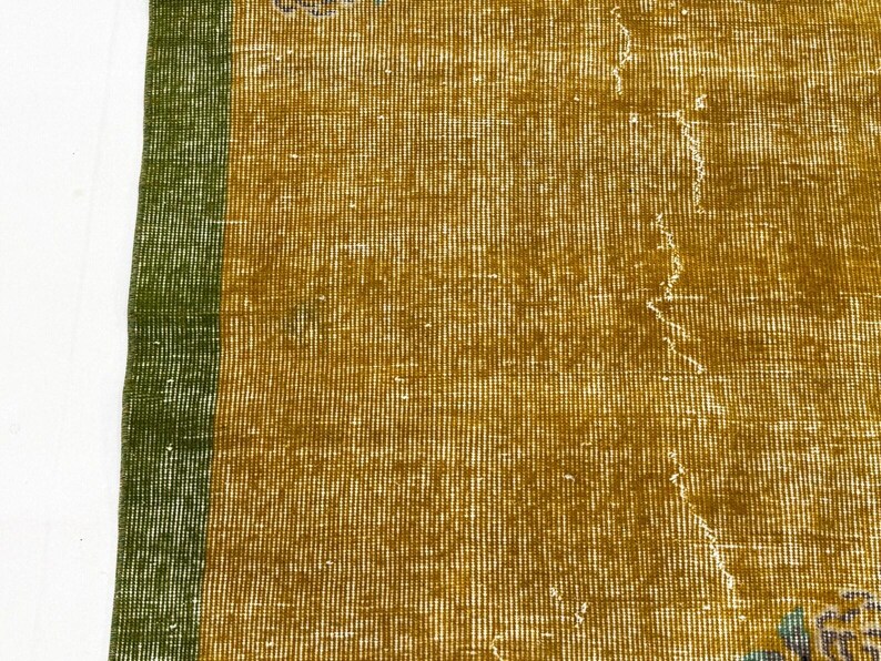 May include: A woven textile rug featuring a mustard yellow central field with a distinct vertical green border along the left edge. The surface displays a visible grid-like weave pattern with subtle signs of wear and light distressing throughout.
