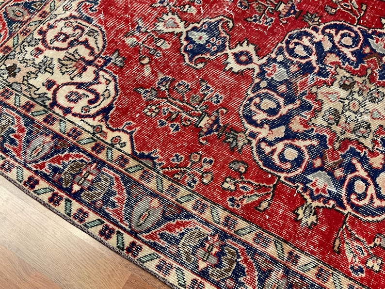 Pu&ograve; includere: Un tappeto rettangolare con uno sfondo rosso vivace e intricati motivi floreali e geometrici in blu profondo, crema e verde chiaro. Il design include un motivo a medaglione centrale e un bordo dettagliato con forme ripetitive.