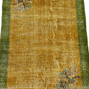 May include: A rectangular runner rug featuring a central mustard yellow field with a distressed texture, flanked by solid green borders on the left and right sides. The rug displays floral motifs in blue and white at the top and bottom corners.