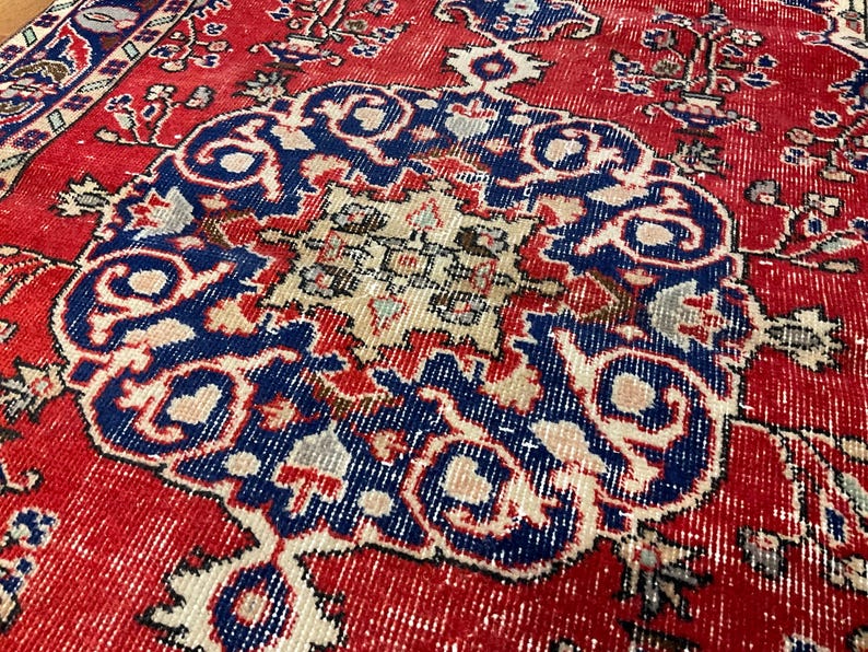 Pu&ograve; includere: Un tappeto rettangolare con uno sfondo rosso vivace e un grande medaglione centrale circolare in blu profondo, crema e azzurro. Il design presenta intricati motivi floreali e geometrici su tutto il campo e lungo i bordi.