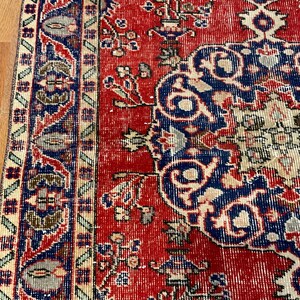 Pu&ograve; includere: Un tappeto rettangolare caratterizzato da un campo rosso vivace con un grande medaglione blu centrale. Il design include intricati motivi floreali e geometrici in tonalit&agrave; crema, blu navy e verde salvia, rifinito con un bordo decorativo.