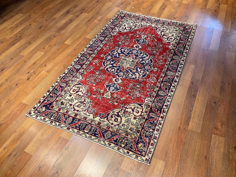 Pu&ograve; includere: Un tappeto rettangolare caratterizzato da un campo centrale rosso vibrante con un prominente medaglione circolare blu scuro. Il tappeto &egrave; decorato con intricati motivi floreali e a viticcio in crema, blu navy e azzurro, incorniciato da un'ampia bordura blu scuro.