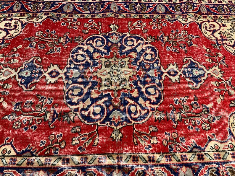 Pu&ograve; includere: Un tappeto rettangolare caratterizzato da un campo rosso vivace con un medaglione centrale blu scuro. Il design include complessi motivi floreali e geometrici in tonalit&agrave; crema, azzurro e blu scuro, rifinito con un bordo dettagliato.