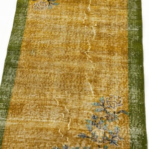May include: A rectangular runner rug featuring a mustard yellow centre field with a distressed texture and faded floral motifs in blue and white. The rug is framed by solid green borders on both long sides, showcasing a worn, vintage appearance.