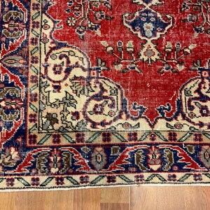 Pu&ograve; includere: Un tappeto rettangolare caratterizzato da un campo centrale rosso vivace con intricati motivi floreali e paisley in blu e crema. Il bordo &egrave; costituito da una fascia blu scuro con motivi geometrici e un bordo esterno color crema con accenti verdi.