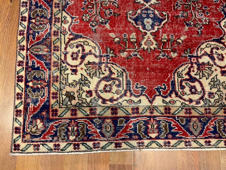 Pu&ograve; includere: Un tappeto rettangolare caratterizzato da un campo centrale rosso vivace con intricati motivi floreali e paisley in blu e crema. Il bordo &egrave; costituito da una fascia blu scuro con motivi geometrici e un bordo esterno color crema con accenti verdi.