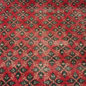 May include: A rectangular rug featuring a repeating geometric pattern of dark green and cream-colored star-like shapes set against a vibrant red background. The textile displays a dense, symmetrical design covering the entire surface area.