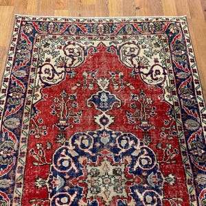 Pu&ograve; includere: Un tappeto rettangolare caratterizzato da un campo centrale rosso vivace con intricati motivi floreali blu e crema. Il tappeto &egrave; incorniciato da un bordo ampio e dettagliato nei toni del blu profondo, rosso e crema, con motivi simmetrici.