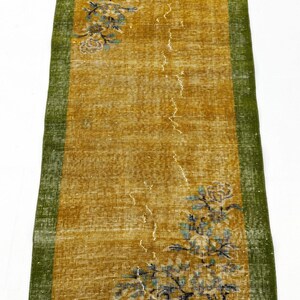 May include: A rectangular runner rug featuring a mustard yellow centre field with a green border. The rug displays floral motifs in shades of blue and white at the top left and bottom right corners, with a distressed texture throughout the surface.