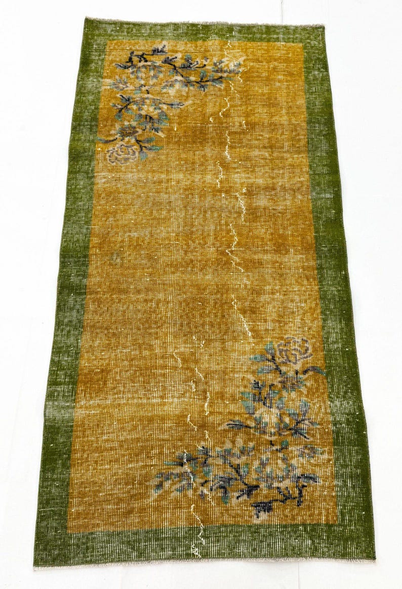 May include: A rectangular runner rug featuring a mustard yellow centre field with a green border. The rug displays floral motifs in shades of blue and white at the top left and bottom right corners, with a distressed texture throughout the surface.