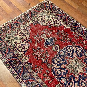 Pu&ograve; includere: Un tappeto rettangolare caratterizzato da un campo centrale rosso vivace con intricati motivi floreali e geometrici in blu e crema. Il tappeto presenta un bordo ampio e dettagliato in tonalit&agrave; blu scuro, rosso e crema, dal design simmetrico.