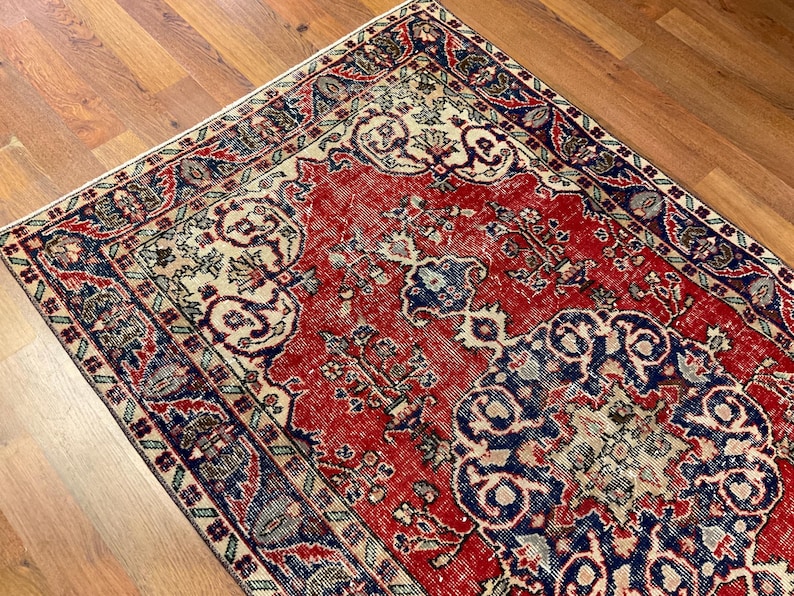 Pu&ograve; includere: Un tappeto rettangolare caratterizzato da un campo centrale rosso vivace con intricati motivi floreali e geometrici in blu e crema. Il tappeto presenta un bordo ampio e dettagliato in tonalit&agrave; blu scuro, rosso e crema, dal design simmetrico.