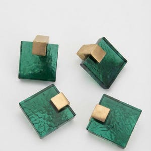 Peut inclure: Quatre pièces décoratives de forme carrée présentant une surface vert émeraude translucide et texturée, associée à un accent en cube de métal doré mat et lisse fixé sur un coin de chaque carré, disposées de manière éparse.