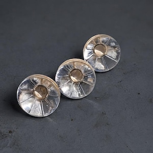 May include: Three circular buttons featuring a clear, transparent glass-like outer rim with a radial, ribbed pattern and a solid, metallic-toned center. The buttons have a smooth, reflective surface and a distinct, layered construction.