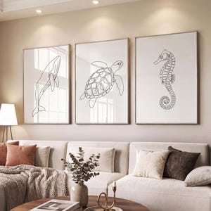 May include: Three framed art prints with line drawings of marine creatures: a whale, a sea turtle, and a seahorse. The black line art is set against a white backdrop. The frames are a light brown colour, creating a minimalist aesthetic.