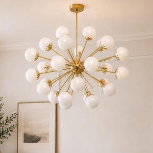 May include: A contemporary living room featuring a gold starburst chandelier with white globe lights. The room includes a beige sectional sofa, a round wooden coffee table, and a cream armchair. A wooden cabinet and framed artwork are also present.