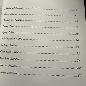 Op de afbeelding: Een inhoudsopgave van een boek met de titel Contents en een naaldgrafiek, met de volgende hoofdstukken: Shades of Lavender 5, Heart Strings 11, Santas on Parade 18, Fancy Fans 29, Zippy Zebra 36, All-American Kids 48, Sailing, Sailing 56, Pine View Cabin 62, American Home 71, Cats 'N Patches 82, General Directions 90.