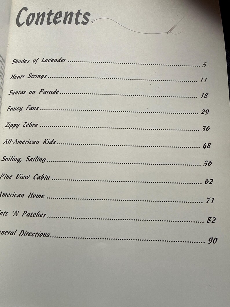 Op de afbeelding: Een inhoudsopgave van een boek met de titel Contents en een naaldgrafiek, met de volgende hoofdstukken: Shades of Lavender 5, Heart Strings 11, Santas on Parade 18, Fancy Fans 29, Zippy Zebra 36, All-American Kids 48, Sailing, Sailing 56, Pine View Cabin 62, American Home 71, Cats 'N Patches 82, General Directions 90.