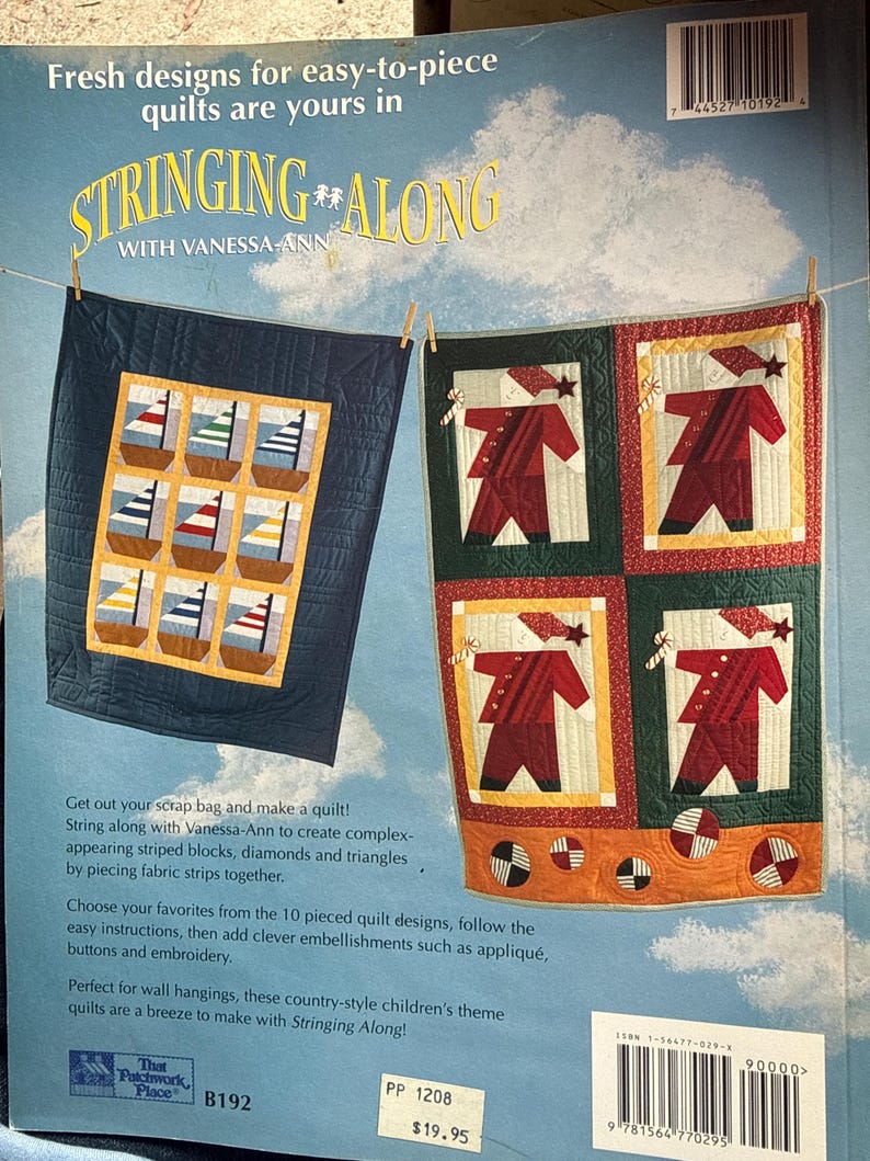 Op de afbeelding: Een instructieboek met zachte kaft getiteld Stringing Along with Vanessa-Ann met twee quilts op de omslag. De ene quilt toont negen zeilbootblokken, terwijl de andere vier kerstmanfiguren laat zien. De achtergrond is een blauwe lucht met wolken.