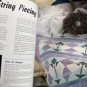 Op de afbeelding: Een boekpagina getiteld String Piecing met tekst over quilttechnieken en een biografie van de ontwerper, naast een doorgestikte sprei met een lichtblauw, paars en wit ruitpatroon met donkergroene bloemmotieven en een krans.